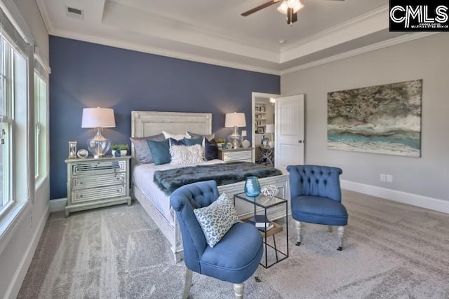 carpeted bedroom featuring ceiling fan, multiple windows, and a raised ceiling