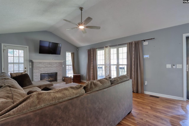 living room with a brick fireplace, ceiling fan, vaulted ceiling, light hardwood / wood-style flooring, and a healthy amount of sunlight