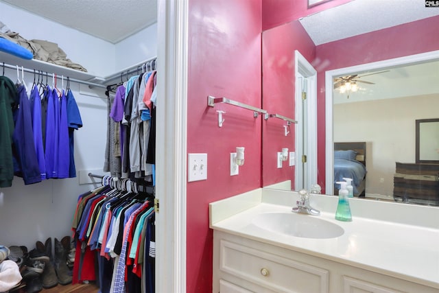 bathroom with ceiling fan, a textured ceiling, and vanity with extensive cabinet space