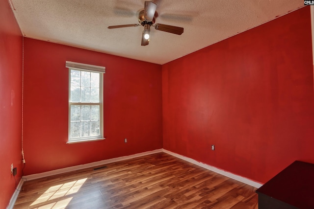 empty room with plenty of natural light, dark wood-type flooring, a textured ceiling, and ceiling fan