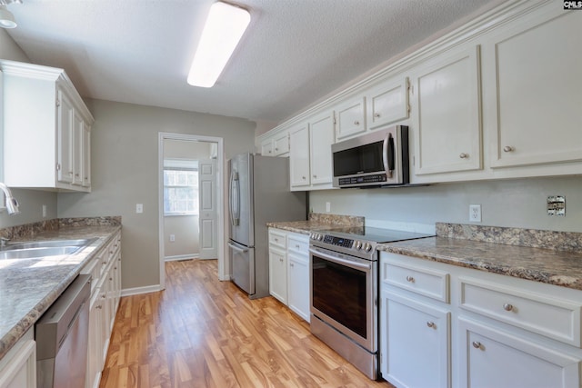 kitchen featuring appliances with stainless steel finishes, light hardwood / wood-style floors, white cabinets, light stone countertops, and sink