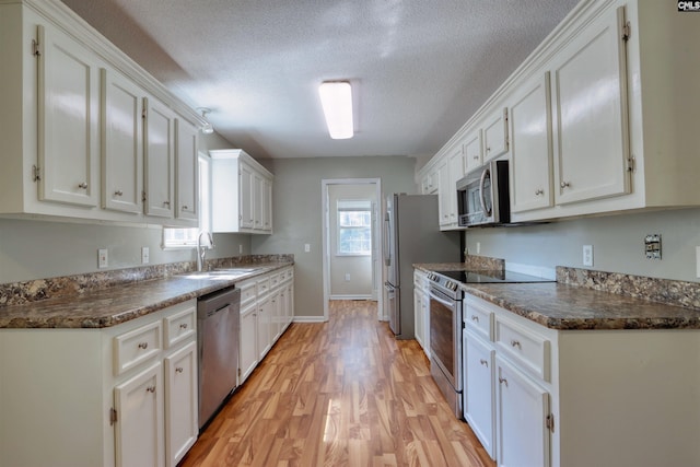 kitchen with appliances with stainless steel finishes, white cabinetry, sink, and light hardwood / wood-style flooring