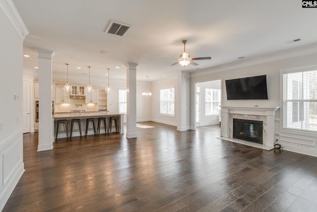 living room featuring dark hardwood / wood-style flooring, ornate columns, crown molding, a high end fireplace, and ceiling fan with notable chandelier