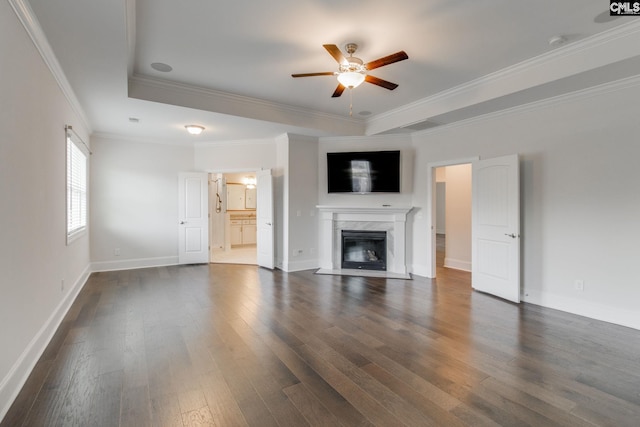 unfurnished living room featuring a tray ceiling, ceiling fan, a premium fireplace, crown molding, and dark hardwood / wood-style flooring