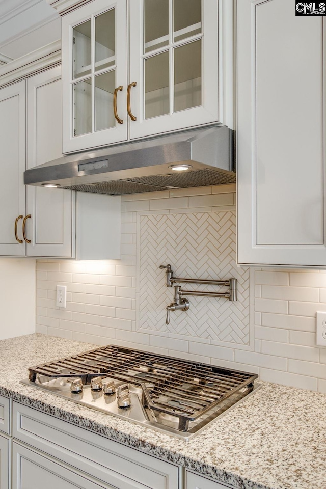 kitchen with white cabinets, tasteful backsplash, fume extractor, and light stone counters