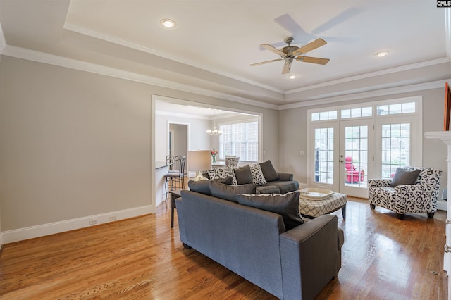 living room featuring a raised ceiling, ornamental molding, light hardwood / wood-style flooring, and ceiling fan with notable chandelier