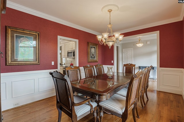 dining area with ornamental molding, a notable chandelier, and light wood-type flooring