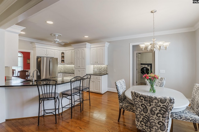 kitchen featuring hanging light fixtures, ceiling fan with notable chandelier, light hardwood / wood-style flooring, crown molding, and stainless steel refrigerator