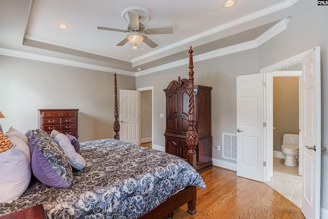 bedroom featuring a tray ceiling, ceiling fan, light hardwood / wood-style floors, ensuite bathroom, and ornamental molding