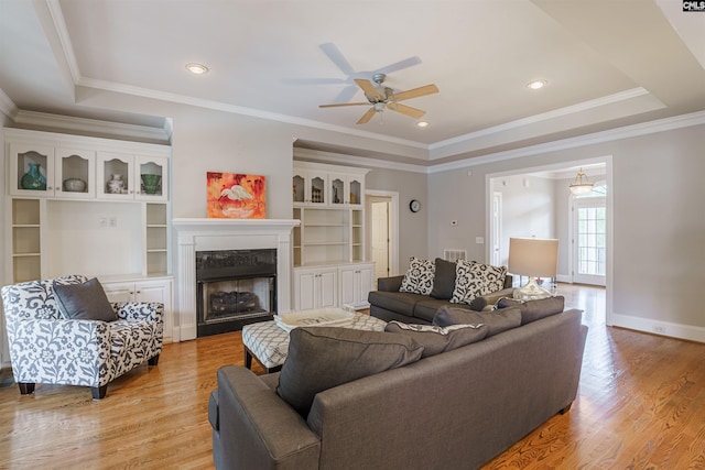 living room featuring light hardwood / wood-style floors, a fireplace, ceiling fan, ornamental molding, and a raised ceiling