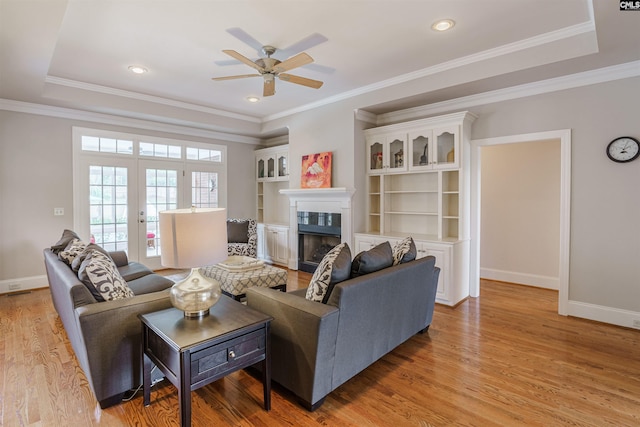 living room with a raised ceiling, light hardwood / wood-style floors, ornamental molding, and ceiling fan