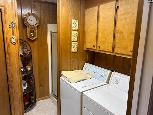 laundry area featuring washing machine and dryer, light colored carpet, wood walls, and cabinets