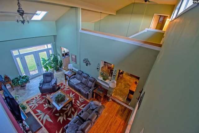 living room with a skylight, ceiling fan, high vaulted ceiling, beam ceiling, and hardwood / wood-style flooring