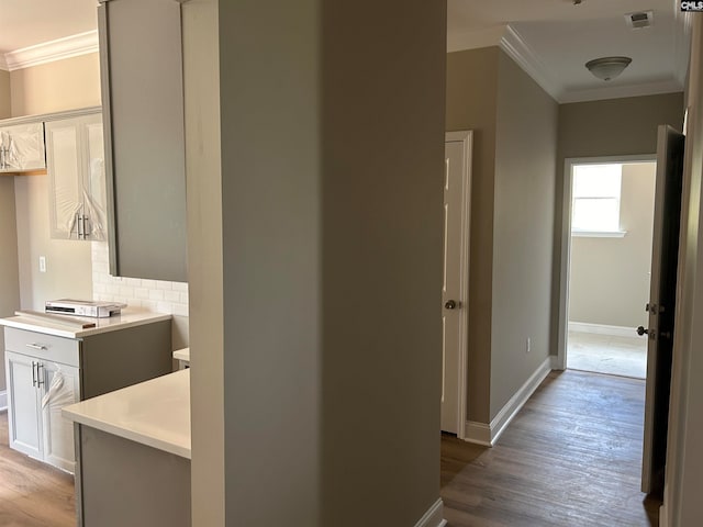 hall with ornamental molding, visible vents, baseboards, and wood finished floors