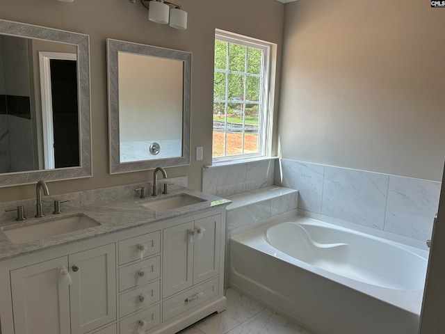 full bath featuring double vanity, marble finish floor, a garden tub, and a sink