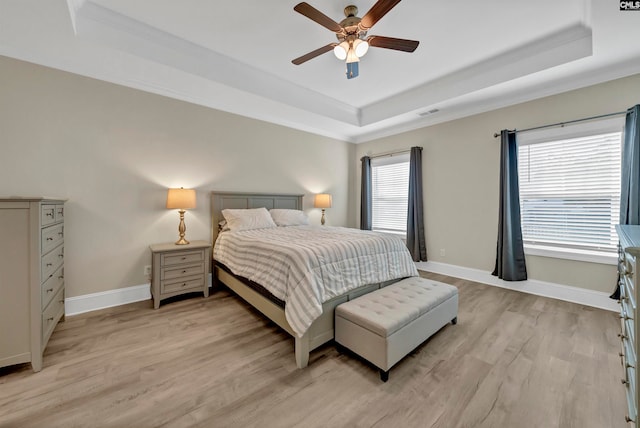 bedroom with wood-type flooring, a raised ceiling, and multiple windows