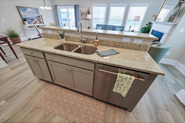 kitchen featuring light stone countertops, light wood-type flooring, pendant lighting, sink, and dishwasher