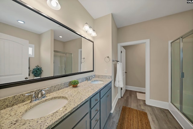 bathroom with wood-type flooring, a shower with door, vanity with extensive cabinet space, and dual sinks