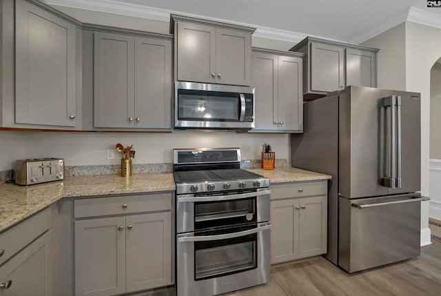 kitchen featuring light hardwood / wood-style flooring, crown molding, light stone counters, gray cabinetry, and appliances with stainless steel finishes