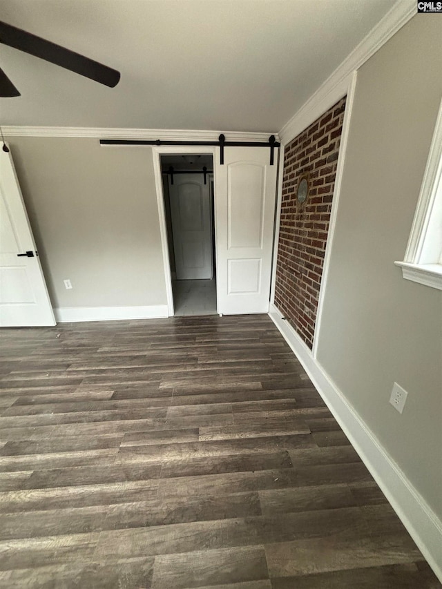 unfurnished bedroom with a barn door, dark hardwood / wood-style flooring, and crown molding