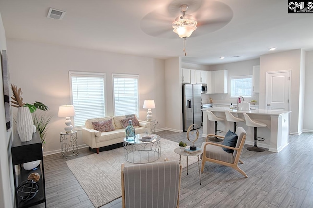 living room with a wealth of natural light, light hardwood / wood-style floors, and ceiling fan