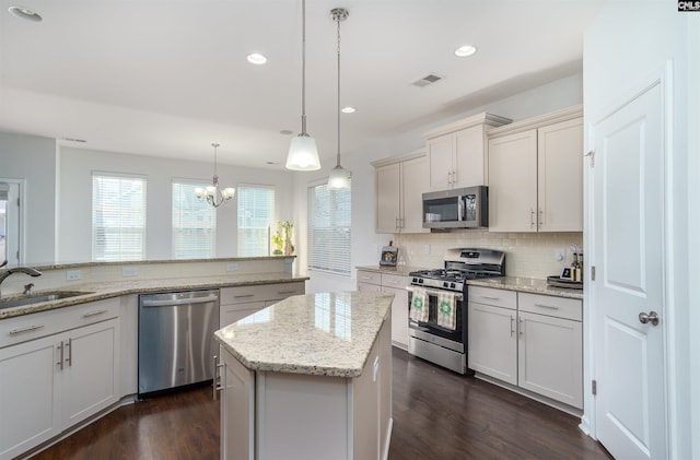 kitchen with decorative light fixtures, an inviting chandelier, dark wood-type flooring, a kitchen island, and stainless steel appliances