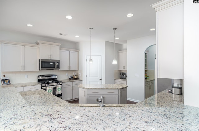 kitchen featuring hanging light fixtures, a kitchen island, light stone counters, stainless steel appliances, and backsplash