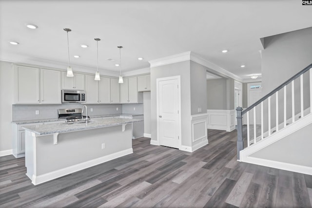 kitchen featuring a center island with sink, light stone countertops, appliances with stainless steel finishes, decorative light fixtures, and dark hardwood / wood-style flooring