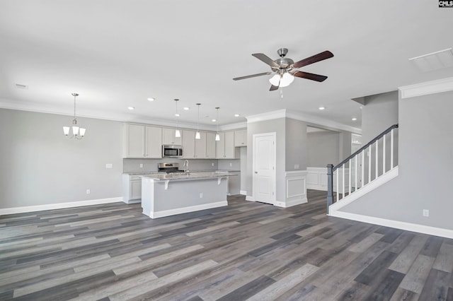 kitchen with dark wood-type flooring, hanging light fixtures, an island with sink, white cabinets, and ornamental molding