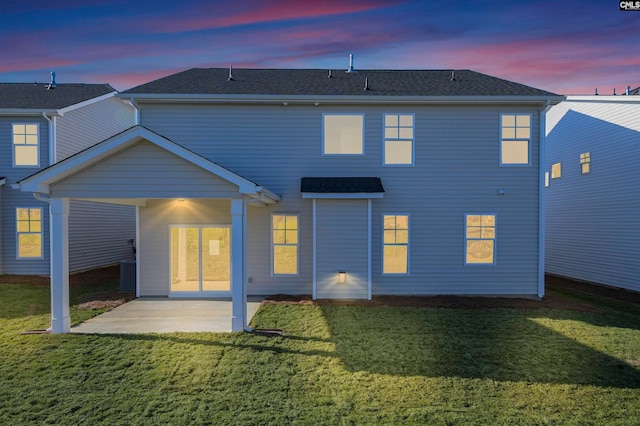 back house at dusk featuring a yard and a patio