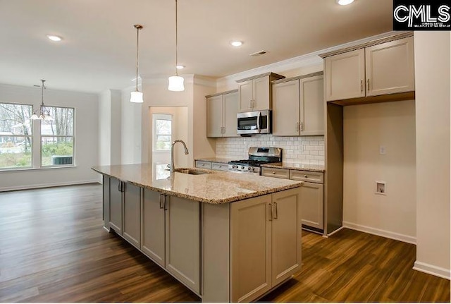 kitchen with sink, hanging light fixtures, light stone counters, a kitchen island with sink, and appliances with stainless steel finishes