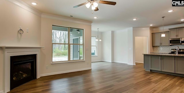 unfurnished living room with dark hardwood / wood-style flooring, ceiling fan with notable chandelier, and ornamental molding