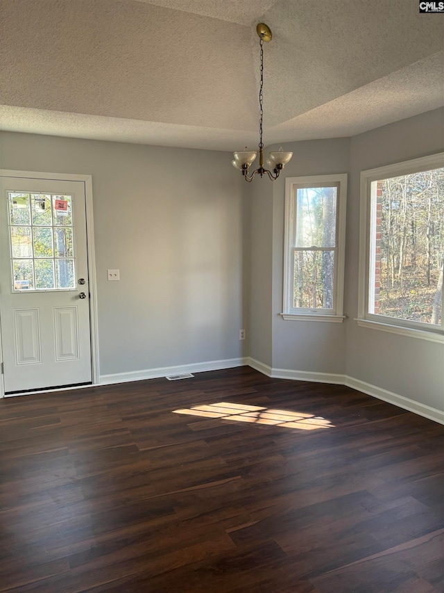 unfurnished dining area with dark hardwood / wood-style floors, an inviting chandelier, and a textured ceiling