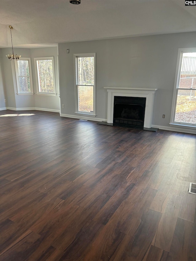 unfurnished living room with a notable chandelier, dark wood-type flooring, and plenty of natural light