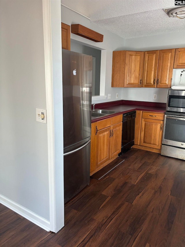 kitchen featuring black dishwasher, sink, dark hardwood / wood-style floors, a textured ceiling, and stainless steel fridge