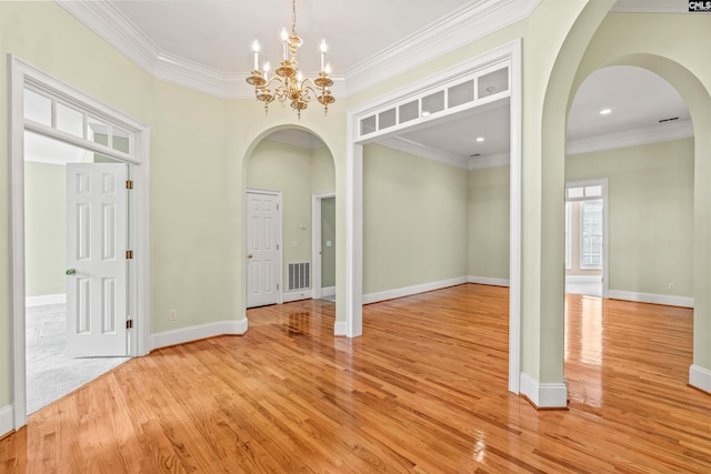 empty room featuring an inviting chandelier, ornamental molding, and light wood-type flooring