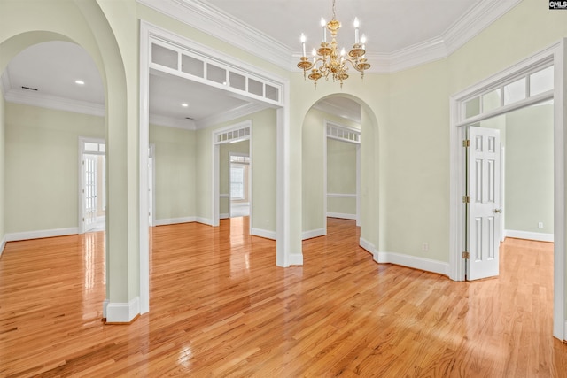 empty room featuring a notable chandelier, ornamental molding, a healthy amount of sunlight, and light hardwood / wood-style floors