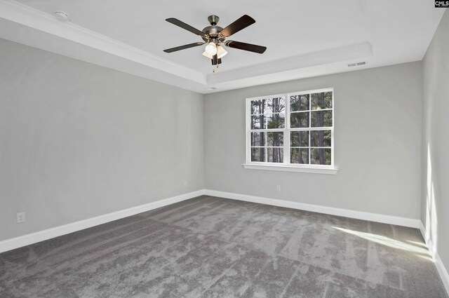 empty room with visible vents, a tray ceiling, dark colored carpet, baseboards, and ceiling fan