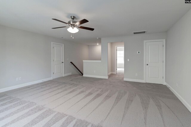 empty room featuring visible vents, light colored carpet, a ceiling fan, and baseboards