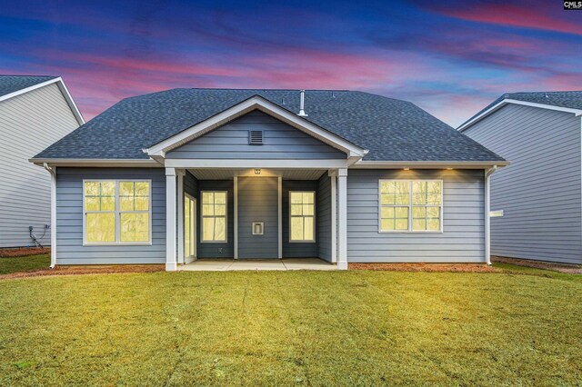 back of property at dusk featuring a patio, a lawn, and a shingled roof