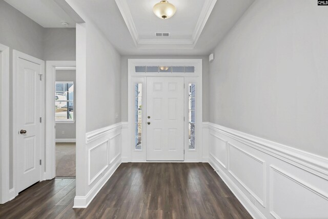 entryway with dark wood-style floors, visible vents, a tray ceiling, crown molding, and a decorative wall