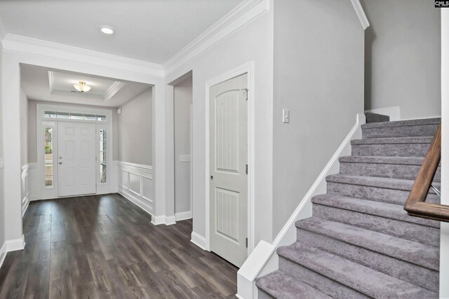 foyer featuring stairway, dark wood-style flooring, a raised ceiling, and ornamental molding