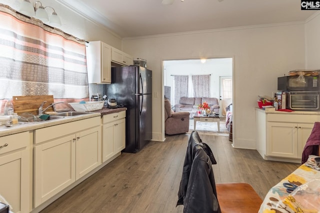 kitchen featuring black refrigerator, ornamental molding, sink, and light wood-type flooring