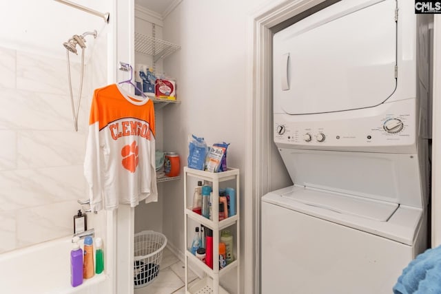 laundry room featuring light tile flooring, crown molding, and stacked washing maching and dryer