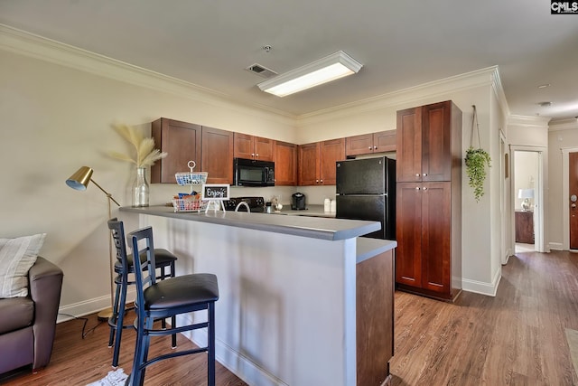 kitchen with dark hardwood / wood-style flooring, a kitchen bar, kitchen peninsula, black appliances, and ornamental molding