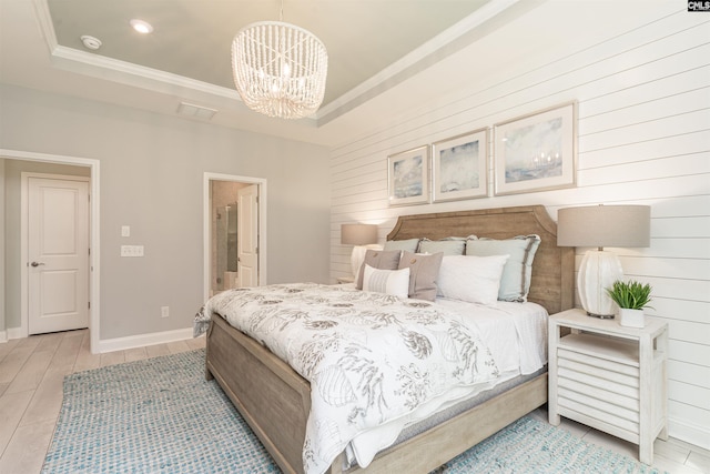 bedroom featuring an inviting chandelier, ensuite bath, crown molding, light wood-type flooring, and a tray ceiling