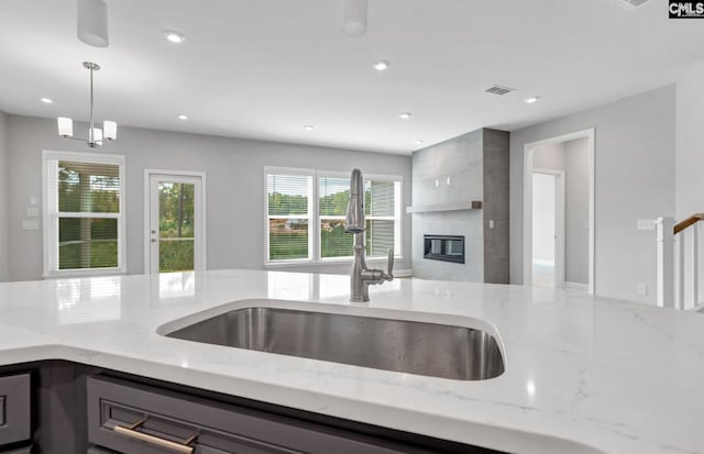 kitchen featuring pendant lighting, sink, light stone counters, and a fireplace