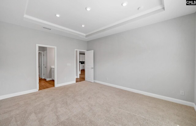 unfurnished bedroom with light carpet, a tray ceiling, and ensuite bathroom