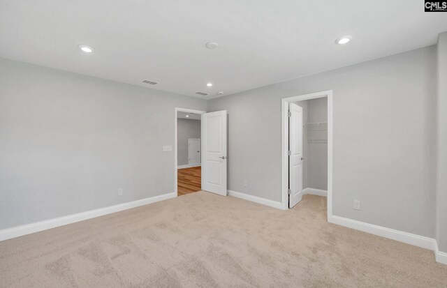 unfurnished bedroom featuring light colored carpet, a spacious closet, and a closet