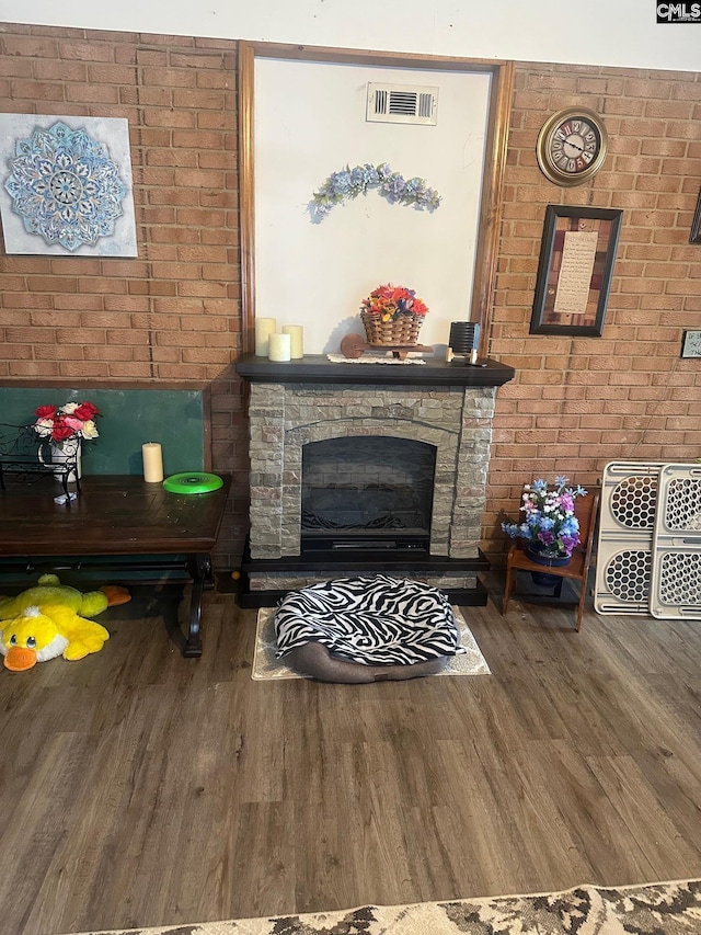 living room with a stone fireplace, brick wall, and hardwood / wood-style flooring